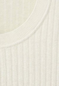 Gros plan d'un tissu côtelé couleur crème avec un col arrondi et une texture fine en tricot.