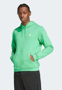 Groene katoenen hoodie met een voorzak en een trekkoord capuchon, voorzien van een klein wit Adidas-logo op de borst. Draag met zwarte broek.
