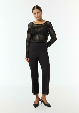 Black sheer long-sleeve top with horizontal striping, paired with high-waisted black trousers and black slingback heels.