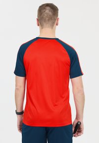 Röd idrottströja med blå raglanärmar, slät textur och korta ärmar. Utrustad med en rundad krage och minimala designelement.