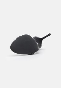 Chaussure à talon hauts noire avec une semelle ovale texturée et une sangle élégante. Elle présente un talon fin et un design minimaliste.