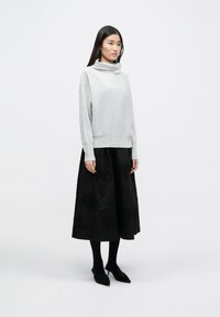 Ανοιχτό γκρι πουλόβερ με λαιμόκοψη cowl, συνδυασμένο με μια μαύρη φούστα που διαθέτει λουλουδάτο κεντήματα από χάντρες, φορεμένο με μαύρες κολάν και παπούτσια.