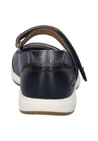 Sandalia de piel negra con acabado texturizado, correa posterior ajustable, talón abierto y suela de goma blanca. Diseño minimalista sin adornos.