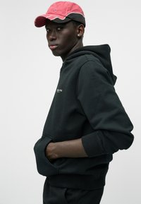 Sweatshirt preto com bolso canguru, punhos canelados e detalhe bordado. Combinado com um boné vermelho com costura em contraste.