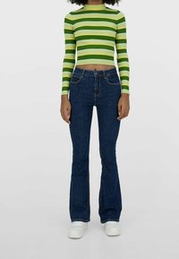 Zielono-biały prążkowany, dzianinowy krótki top z długim rękawem, zestawiony z ciemnoniebieskimi dzwonami z wysokim stanem i białymi trampkami.