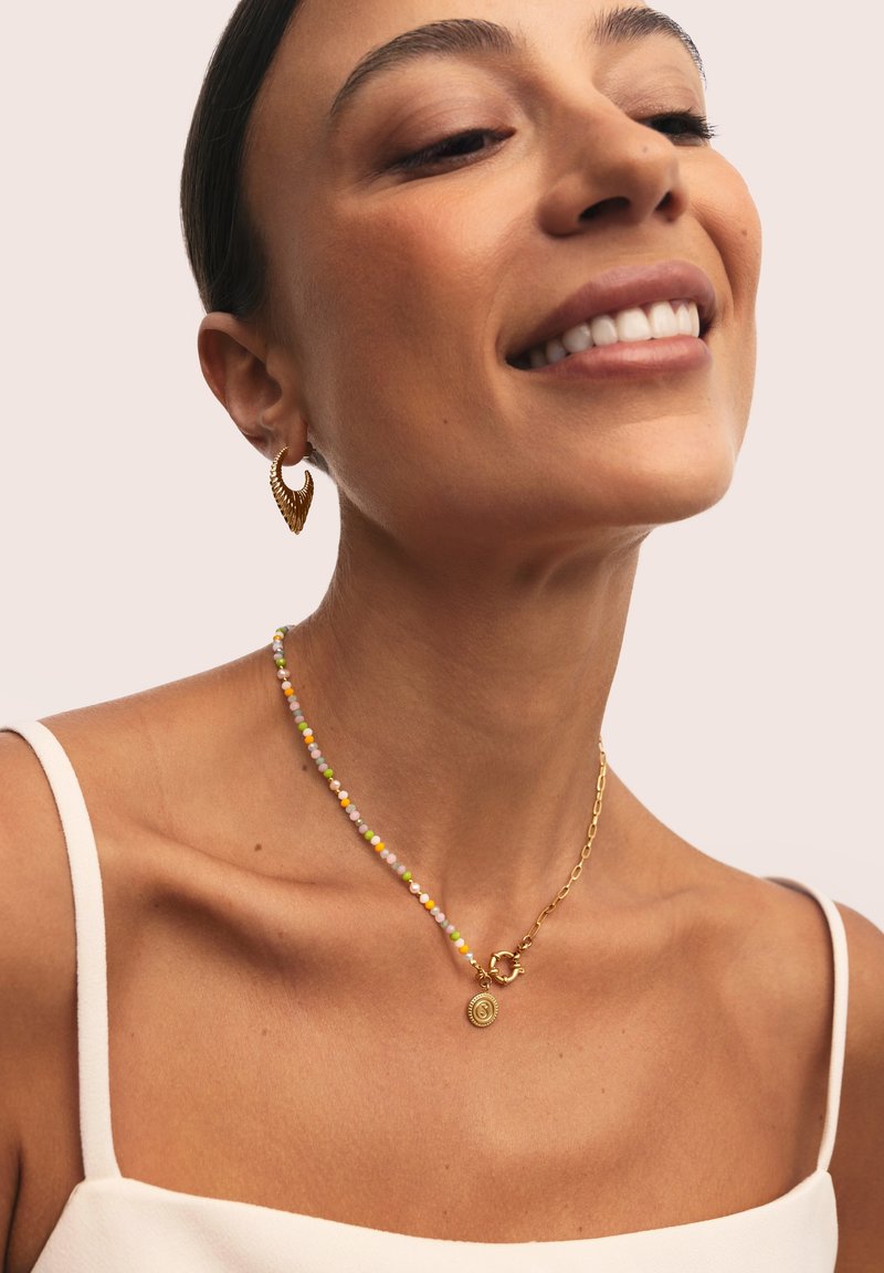 Orecchini color oro e una collana di perline con perline color pastello e un dettaglio pendente circolare; indossati contro la pelle nuda.