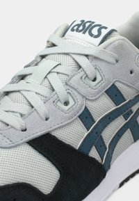 Szare trampki wykonane z siateczki i zamszu, z ciemnoniebieskimi akcentami oraz białą podeszwą środkową, teksturowanymi sznurówkami i logo na języku.