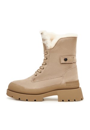 Botte d'hiver beige en daim à lacets, avec semelle en caoutchouc épaisse, doublure en peau de mouton et détail de sangle à pression autour de la cheville.