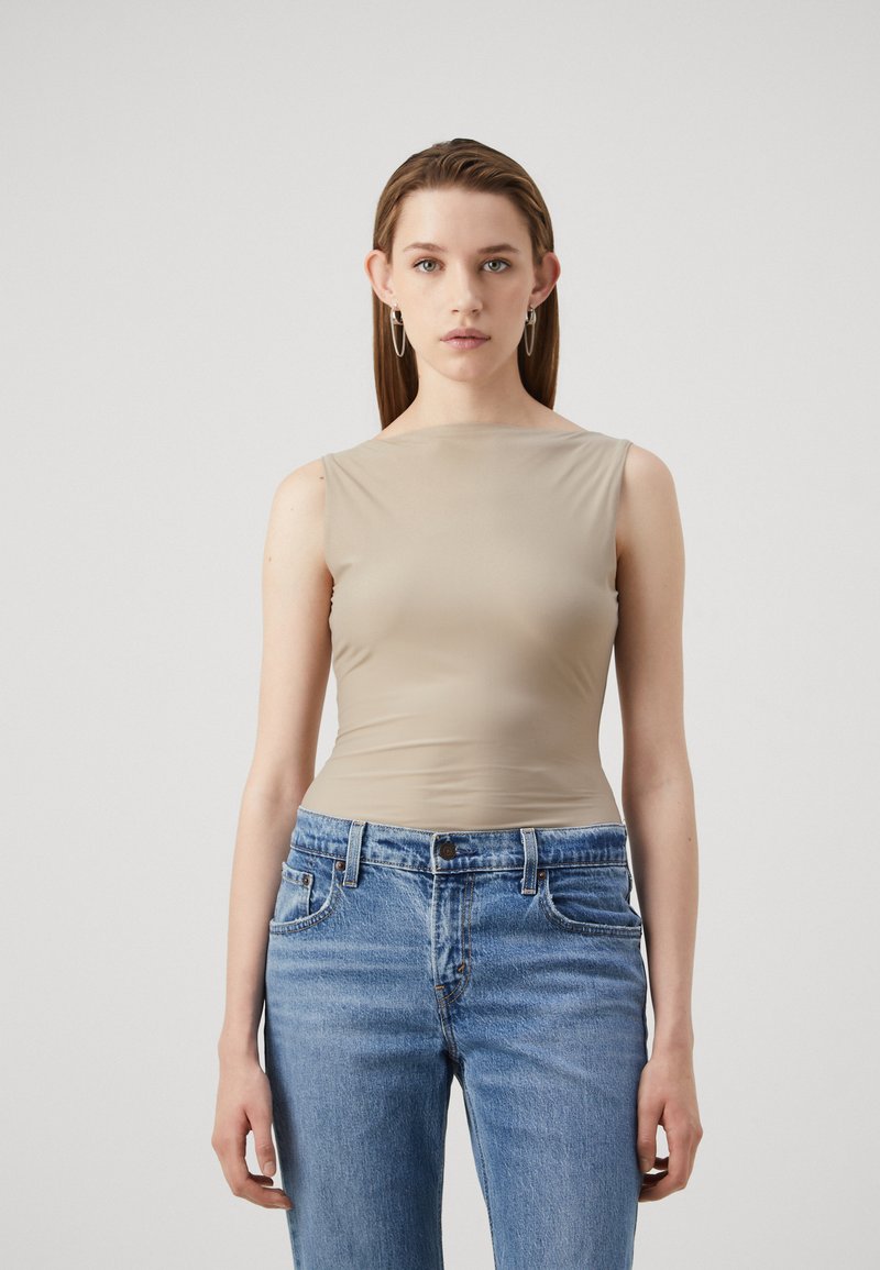Un haut beige sans manches, au design ajusté en tissu lisse, associé à un jean en denim bleu clair. Lignes simples et épurées avec des textures subtiles.