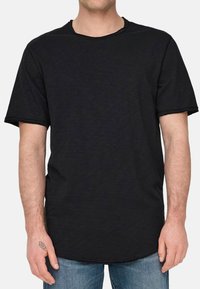 T-shirt nera a maniche corte con scollatura rotonda, caratterizzata da un orlo leggermente curvo e bordi grezzi. Realizzata in un tessuto morbido e testurizzato.