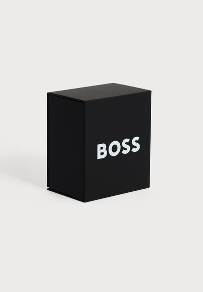 Boîte rectangulaire noire avec le mot "BOSS" en lettres majuscules blanches sur le devant, sur un fond clair uni.