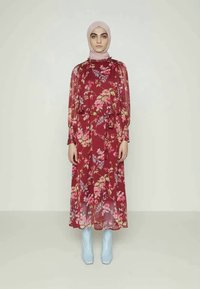 Vestido floral vermelho com mangas longas e transparentes e cintura com laço. Combinado com botas de plataforma azul claro. O tecido apresenta padrões de flores vibrantes.
