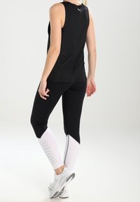 Svart atletisk linne kombinerat med åtsittande svarta tights med vita detaljer och "PUMA"-logotyp, kompletterat med vita sneakers.