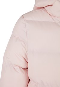 Ljusrosa pufferjacka med en kviltad design, mjuk vaddering, huva och en len textur. Synlig söm längs sömmarna.