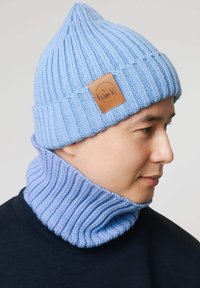 Jasnoniebieska dziana czapka z prążkowaną fakturą i skórzaną naszywką. W zestawie z dopasowanym jasnoniebieskim, prążkowanym kominowym szalikiem, oba miękkie i ciepłe.