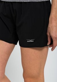 Bermudas deportivas negras con una cintura elástica, que presentan un sutil logo "Venice Beach" en blanco cerca del dobladillo, textura de tela suave.