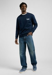 Navyblauwe sweatshirt met wit "Lee" logo, ronde halslijn, gecombineerd met lichtblauwe jeans en grijze sneakers, met een ontspannen pasvorm.