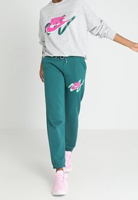 Mörkgröna joggers med elastiska cuffs har en rosa Nike-logotyp. Kan kombineras med en grå sweatshirt som visar en färgglad Nike-grafik.