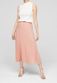 Gonna midi plissettata rosa chiaro abbinata a un top senza maniche bianco. Il top presenta bordi ondulati e una trama a maglia liscia.