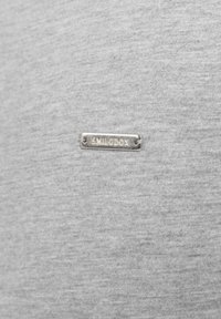 Camicia in cotone grigia con una texture liscia, caratterizzata da una piccola placca logo argentata con la scritta "SMILODOX" cucita nel tessuto.