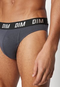 Graue Baumwollslips mit einem schwarzen Bund, der "DIM" in weißen Buchstaben zeigt. Glatte Textur, konturiertes Design für Komfort und Passform.