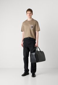 Tricou din bumbac bej cu un buzunar, blugi din denim negri și o geantă din piele neagră cu mânere. Pantofii negri completează ținuta.