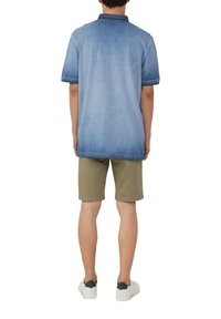 Denimowa koszula polo w jasnoniebieskim gradiencie, z kołnierzykiem wykończonym ciemnym obszyciem, w zestawie z jasnymi szortami w kolorze khaki i białymi sneakersami. Tekstura wydaje się gładka.