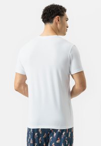 Witte t-shirt met korte mouwen en ronde hals, gemaakt van zachte katoenstof, weergegeven vanuit de achterkant, gecombineerd met gestreepte pyjamabroek.