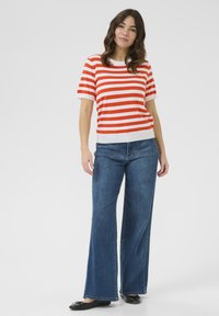 Pull à manches courtes rayé rouge et blanc avec une coupe décontractée, associé à un jean en denim bleu à jambes larges et des chaussures plates noires.