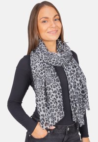 Écharpe imprimé léopard en gris et noir, fabriquée en tissu léger avec des bords effilochés, drapée élégamment autour du cou.