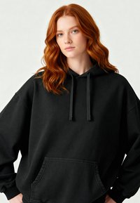 Felpa nera oversize realizzata in morbido tessuto, con tasca frontale, lacci al collo e polsini a costine.