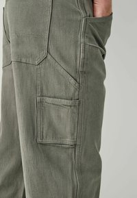 Khaki cargo pants featuring a durable fabric, side pocket, structured seams, and a relaxed fit with a textured surface.