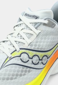 Sive mrežaste tenisice za trčanje s bijelim vezicama, reflektirajućim detaljima i gradijentnom potplatom koja prelazi iz žute u narančastu.