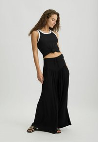 Czarny crop top z białym wykończeniem, zawiązany w talii, w połączeniu z szerokimi czarnymi spodniami z elastycznym pasem. Czarne sandały.