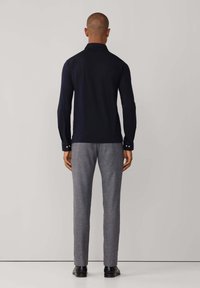 Mornarska košulja dugih rukava s kragnom, u kombinaciji s svijetlosivim hlačama. Glatka tkanina s kopčama na manžetama.