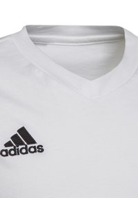 Weißes Baumwoll-T-Shirt mit V-Ausschnitt, versehen mit einem schwarzen gestickten Adidas-Logo auf der unteren linken Seite. Glatte Textur, lässiges Design.