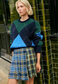 Pull en argyle bleu, vert et marine à manches longues ; jupe plissée à carreaux dans des teintes de bleu, jaune et vert, présentant plusieurs motifs.