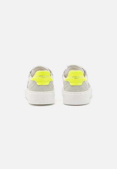 Weiße niedrige Sneakers aus Leder mit grauen Wildlederakzenten, sichtbar gepolstertem Schaft und leuchtend gelbem Fersenstück mit eingestanztem Markenlogo.