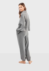 Šedá oříznutá mikina s límečkem v kombinaci s odpovídajícími tepláky. Má elastické manžety a volný střih. Bez viditelných vzorů.