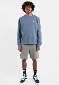 Sweat-shirt bleu clair avec col rond, short gris, chaussettes rayées noires et blanches, et baskets montantes noires à semelles blanches.