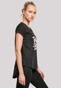 Black cotton t-shirt with short sleeves, featuring a stylized logo in light blue and pink. Hemline is longer at the back for a relaxed fit.
