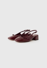 Chaussures slingback en cuir verni bordeaux avec un bout rond, un petit talon carré et un détail de nœud décoratif sur la sangle supérieure.