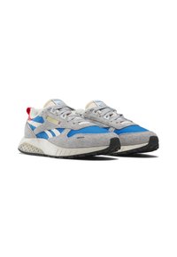 Un par de zapatillas Reebok en gris y azul con rayas blancas, suelas beige y lengüetas traseras rojas sobre un fondo blanco.