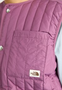 Ljuslila vadderad väst med ficka fram och tryckknappsstängning. Har en märkespåtagning och en slät tygtextur.