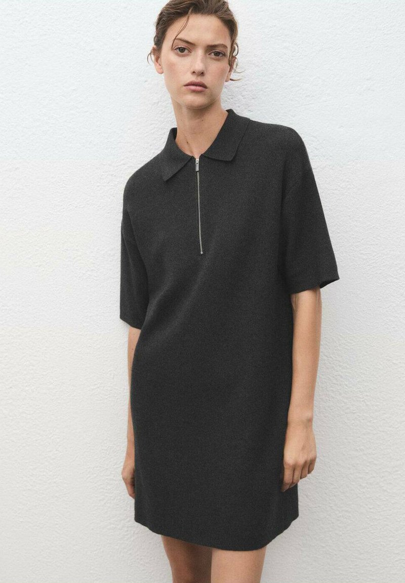 Black dress made of soft fabric, featuring a classic collar, short sleeves, and a front zipper detail. Minimalist design and streamlined silhouette.