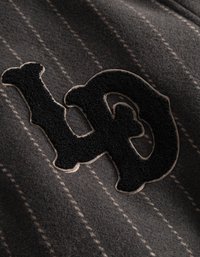 Grijze stof met fijne verticale strepen. Prominente zwarte applicatie met een cirkelontwerp en randen omlijnd in een lichte kleur.