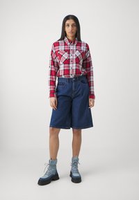 Chemise à manches longues à carreaux rouges et blancs avec poches poitrine, assortie à un short en denim bleu et des bottes à lacets bleu clair avec de grosses semelles noires.