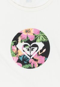 T-shirt bianco con una grafica circolare caratterizzata da motivi floreali rosa e verdi che circondano un logo a forma di cuore in bianco e nero al centro.