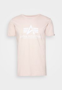 Světle růžové bavlněné tričko s krátkými rukávy, na přední straně s bílým grafickým logem "Alpha Industries" a geometrickými vzory.