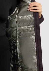 Giacca a vento scura con imbottitura trapuntata e rivestimento argentato metallico. Presenta una tasca laterale sul rivestimento.